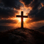 A rugged wooden cross silhouetted against a dramatic sunset sky on a hilltop, with warm light breaking through clouds—symbolizing both sacrifice and hope.